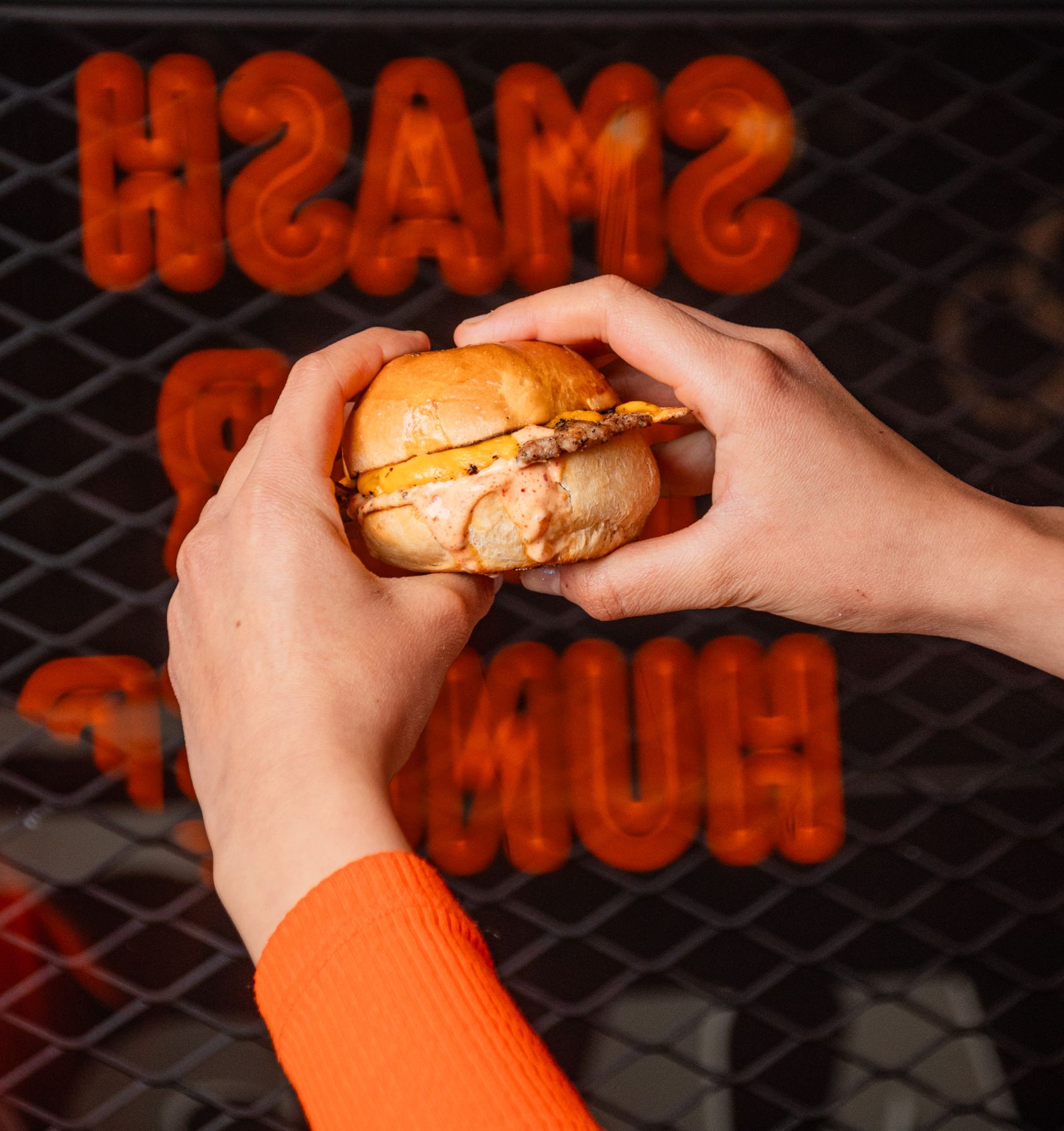 Mão segurando um smash burger na frente de um letreiro neon
